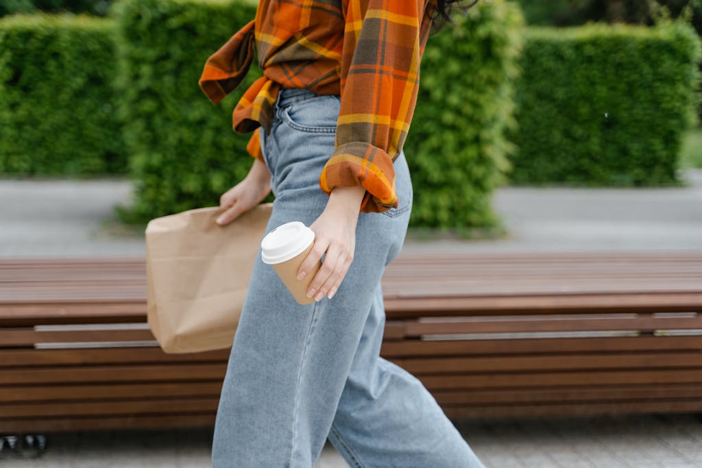 Person in Blue Denim Jeans and Orange Plaid Shirt Sitting on Brown Wooden Bench